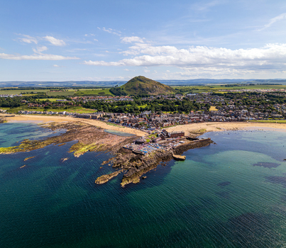 Aerial view of North Berwick Law overlooking the coastal town harbor sandy beach and clear blue sea in North Berwick Scotland United Kingdom. Aerial view of North Berwick Law overlooking the coastal town harbor sandy beach and clear blue sea in North Berwick Scotland United Kingdom.