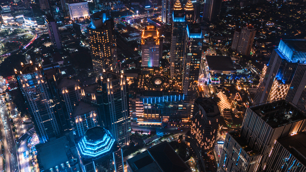Aerial view of the illuminated Jakarta skyline at night featuring modern skyscrapers glowing office buildings and busy city streets with traffic lights in Jakarta Indonesia.