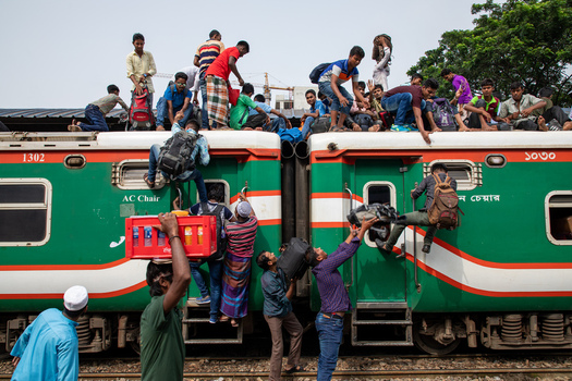 Dhaka Bangladesh 14 June 2018 View of passengers climbing onto the roof and hanging from the doors of a crowded green and red train at Airport Railway Station. Dhaka Bangladesh 14 June 2018 View of passengers climbing onto the roof and hanging from the doors of a crowded green and red train at Airport Railway Station.