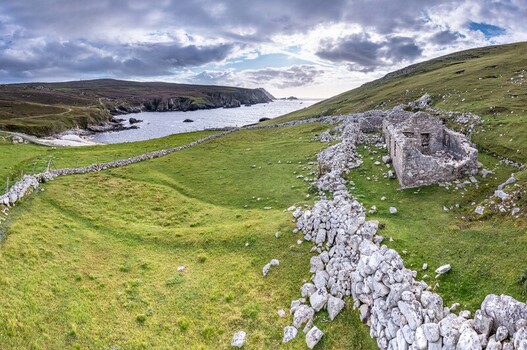 Aerial view of the historic stone ruins of An Port nestled in a green coastal landscape with dry stone walls and cliffs overlooking the Atlantic Ocean in Ardara County Donegal Ireland.