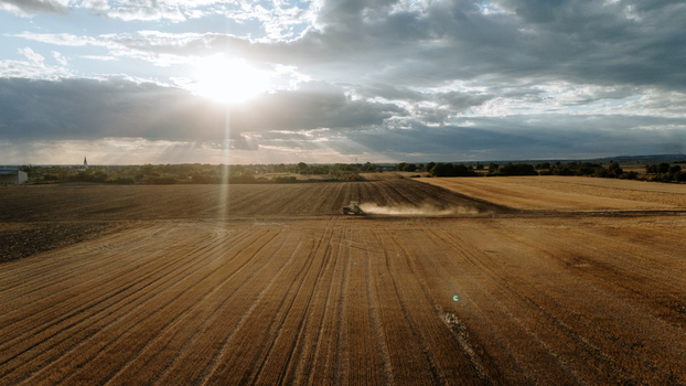 Aerial view of a tractor working in a harvested field with dust rising under a dramatic sunset sky in Veliki Radinci Vojvodina Serbia. Aerial view of a tractor working in a harvested field with dust rising under a dramatic sunset sky in Veliki Radinci Vojvodina Serbia.