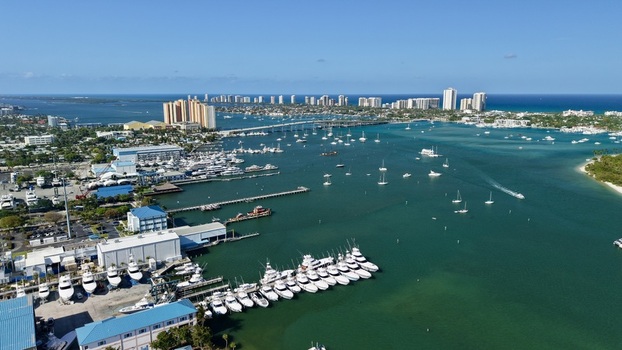 Aerial view of the Riviera Beach Marina Village featuring numerous yachts docked along the pier and a bridge spanning the turquoise coastal waters under a clear blue sky Riviera Beach Florida United States. Aerial view of the Riviera Beach Marina Village featuring numerous yachts docked along the pier and a bridge spanning the turquoise coastal waters under a clear blue sky Riviera Beach Florida United States.