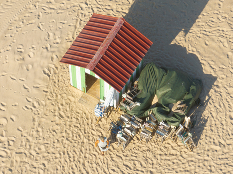 Figueira da Foz Portugal 08 August 2024 Aerial view of Praia da Figueira da Foz featuring a striped beach hut with a red roof stacked chairs and a person walking on the sand.