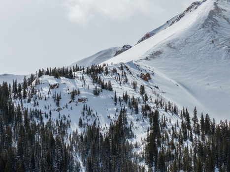 View of snow covered mountain slopes with dense evergreen forests and rocky ridges under a bright sky Colorado United States.