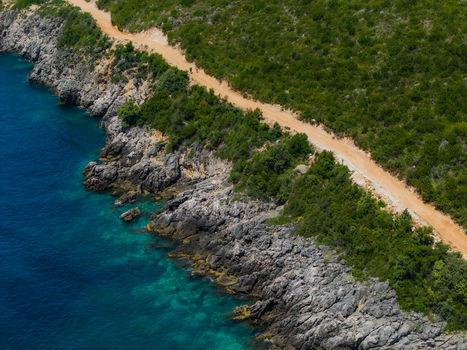 Aerial view of the rugged coastline near Aquarium Beach with a dirt road winding through lush green vegetation and turquoise water in Jala Vlore County Albania. Aerial view of the rugged coastline near Aquarium Beach with a dirt road winding through lush green vegetation and turquoise water in Jala Vlore County Albania.