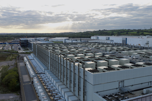 Aerial view of a large data center with numerous cooling units on the roof set in an industrial landscape under a sunset sky in the United Kingdom.