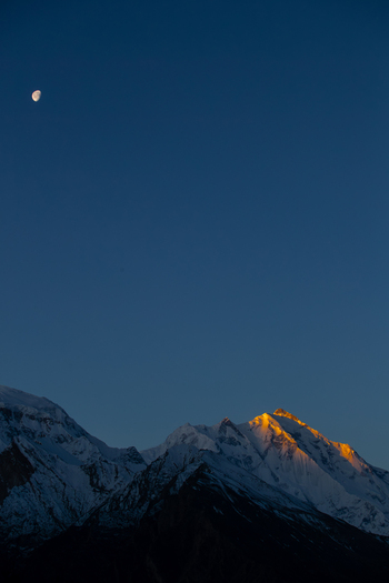 View of the snow capped Rakaposhi mountain peak glowing in golden sunset light under a crescent moon and deep blue sky Hunza Nagar Gilgit Pakistan. View of the snow capped Rakaposhi mountain peak glowing in golden sunset light under a crescent moon and deep blue sky Hunza Nagar Gilgit Pakistan.