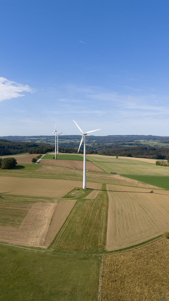 Aerial view of Windpark Eppenrod featuring white wind turbines standing in vast agricultural fields under a clear blue sky in Eppenrod Rheinland Pfalz Germany.