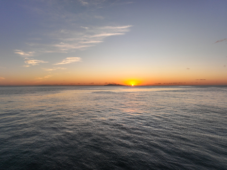 Aerial view of the calm ocean at sunrise with a distant island silhouette on the horizon in Whiritoa Waikato Region New Zealand.
