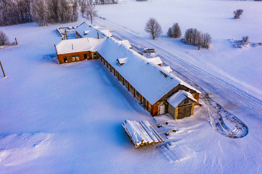 Aerial view of a long brick building surrounded by a vast snow covered landscape with a pile of logs in the foreground and a road in Latvia. Aerial view of a long brick building surrounded by a vast snow covered landscape with a pile of logs in the foreground and a road in Latvia.