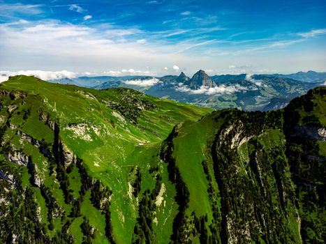 Aerial view of verdant mountain slopes cascading towards distant peaks under a sky brushed with wispy clouds Morschach Schwyz Switzerland. Aerial view of verdant mountain slopes cascading towards distant peaks under a sky brushed with wispy clouds Morschach Schwyz Switzerland.