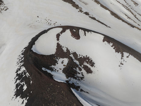 Aerial view of the snow covered volcanic crater on the south slope of Mount Etna with dark volcanic ash and rocky ridges in Nicolosi Sicilia Italy. Aerial view of the snow covered volcanic crater on the south slope of Mount Etna with dark volcanic ash and rocky ridges in Nicolosi Sicilia Italy.