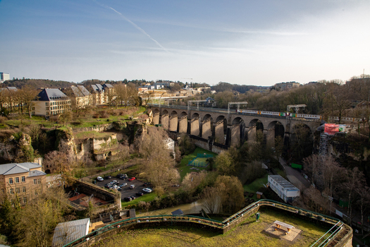 Aerial view of the historic stone viaduct spanning the valley with residential buildings lush greenery and a train crossing the bridge in Luxembourg Luxembourg Luxembourg.
