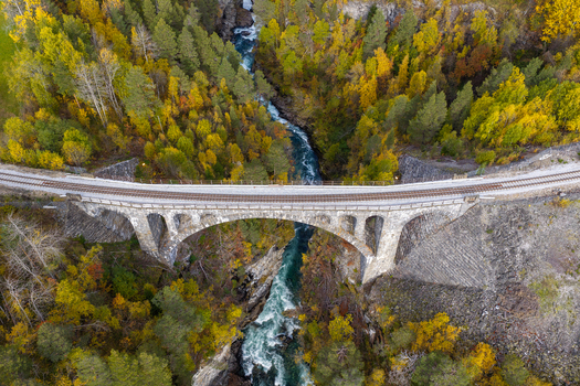 Aerial view of the historic stone arch Kylling Bridge spanning the Rauma River surrounded by vibrant autumn forest in Verma More og Romsdal Norway. Aerial view of the historic stone arch Kylling Bridge spanning the Rauma River surrounded by vibrant autumn forest in Verma More og Romsdal Norway.