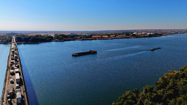 Aerial view of the Danube river with barges navigating the water a busy bridge with heavy traffic and industrial facilities in Smederevo Podunavlje District Serbia.