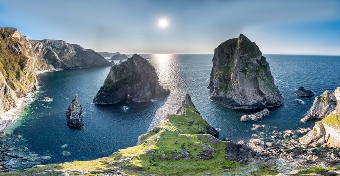 Aerial view of Glenlough Bay featuring dramatic sea stacks and rugged cliffs rising from the Atlantic Ocean under a bright sun in Ardara County Donegal Ireland.