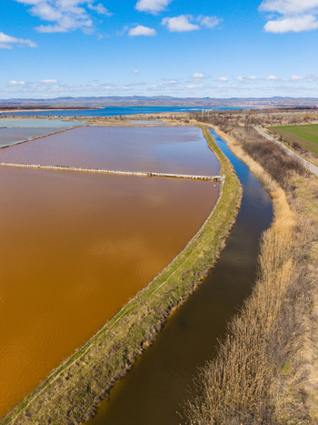Aerial view of the pink salt evaporation ponds of Lake Atanasovsko with a narrow canal and dry vegetation under a blue sky in Burgas Burgas Bulgaria. Aerial view of the pink salt evaporation ponds of Lake Atanasovsko with a narrow canal and dry vegetation under a blue sky in Burgas Burgas Bulgaria.