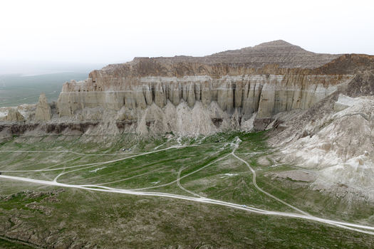 Aerial view of the dramatic limestone cliffs of Airakty surrounded by green grassy plains and dirt tracks in Shetpe Mangystau Region Kazakhstan.