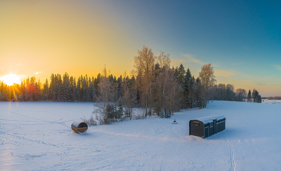 Aerial view of a snowy landscape featuring a barrel sauna and a modern cabin near a forest during a golden sunset Latvia. Aerial view of a snowy landscape featuring a barrel sauna and a modern cabin near a forest during a golden sunset Latvia.