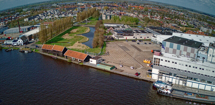 Wormer Netherlands 10 April 2026 Aerial view of a red Electric pusher tug carrying white containers with batteries docked beside the Olam International Cacoa factory contrasting with the dark water. Wormer Netherlands 10 April 2026 Aerial view of a red Electric pusher tug carrying white containers with batteries docked beside the Olam International Cacoa factory contrasting with the dark water.