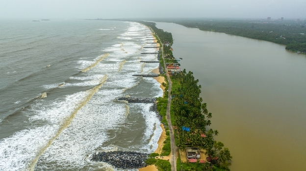 Aerial view of Mattu Beach featuring a narrow strip of land separating the sea from backwaters with stone breakwaters palm trees and a coastal road in Udupi Karnataka India.