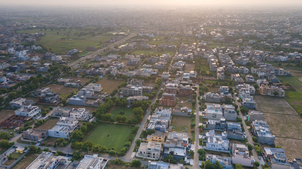 Aerial view of a residential neighborhood with suburban houses green lawns and paved streets under a soft golden hour light in Lahore Punjab Pakistan.