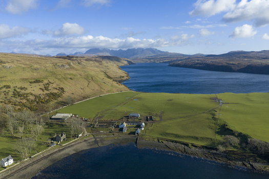 Aerial view of Gesto Bay Viewpoint with green pastures farm buildings and the Cuillin mountains under a blue sky Isle of Skye Scotland United Kingdom.