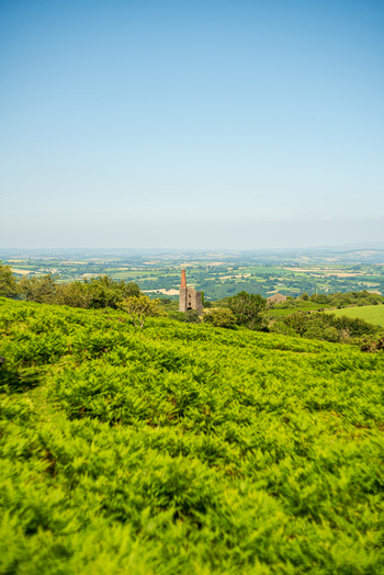 View of the historic Cheesewring landmark set amidst the lush green moorland landscape under a clear blue sky in Minions Cornwall United Kingdom. View of the historic Cheesewring landmark set amidst the lush green moorland landscape under a clear blue sky in Minions Cornwall United Kingdom.