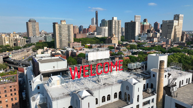 Aerial view of the iconic WELCOME sign atop a building in Brooklyn with the city skyline in the background under a clear blue sky New York New York United States.