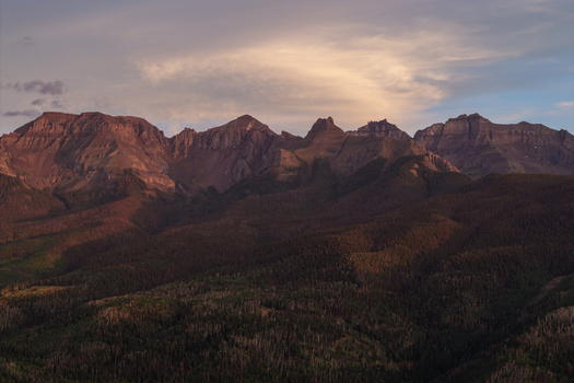 Aerial view of Mount Sneffels in the San Juan Mountain Range featuring rugged peaks dense evergreen forests and soft golden hour light in Ouray Colorado United States. Aerial view of Mount Sneffels in the San Juan Mountain Range featuring rugged peaks dense evergreen forests and soft golden hour light in Ouray Colorado United States.