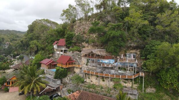 Aerial view of Indrayanti Beach featuring wooden villas with red roofs nestled on a lush green hillside overlooking the coastal landscape in Kecamatan Tepus Daerah Istimewa Yogya Indonesia. Aerial view of Indrayanti Beach featuring wooden villas with red roofs nestled on a lush green hillside overlooking the coastal landscape in Kecamatan Tepus Daerah Istimewa Yogya Indonesia.