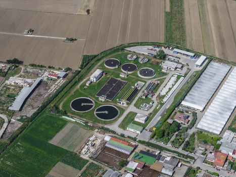 Aerial view of a water treatment plant with circular sedimentation tanks and rectangular basins surrounded by green fields and greenhouses in Paestum Campania Italy.