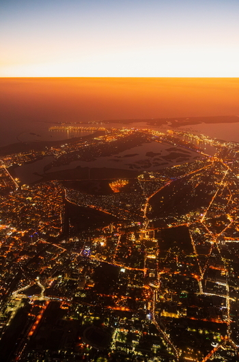 Aerial view of the illuminated cityscape at night featuring glowing street lights urban infrastructure and the coastline under a sunset sky in Karachi Sindh Pakistan.