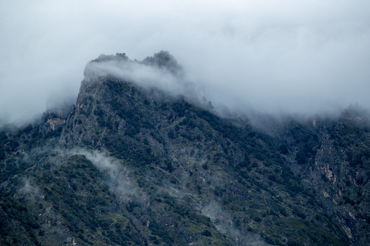 View of rugged mountain peaks partially covered by thick mist and low clouds with sparse green vegetation on the rocky slopes Chilas Gilgit Pakistan. View of rugged mountain peaks partially covered by thick mist and low clouds with sparse green vegetation on the rocky slopes Chilas Gilgit Pakistan.