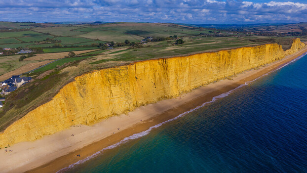 Aerial view of the golden sandstone cliffs of West Bay along the Jurassic Coast with a sandy beach turquoise sea and rolling green hills in West Bay England United Kingdom. Aerial view of the golden sandstone cliffs of West Bay along the Jurassic Coast with a sandy beach turquoise sea and rolling green hills in West Bay England United Kingdom.