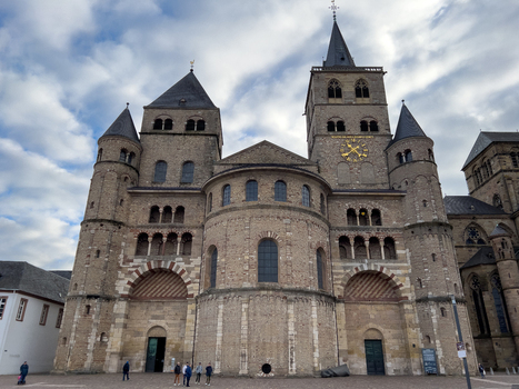 View of the historic Trier Cathedral with its Romanesque and Gothic architecture stone facade arched doorways and clock tower under a cloudy sky in Trier Rheinland Pfalz Germany.