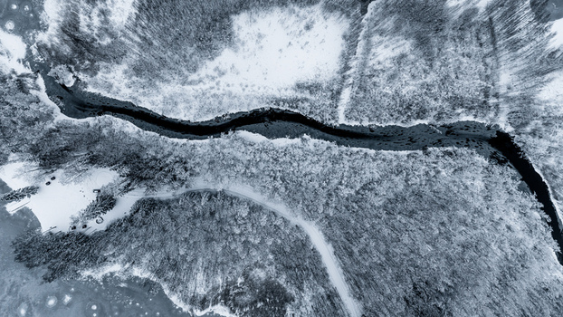 Aerial view of a winding river flowing through a dense snow covered forest landscape in Latvia. Aerial view of a winding river flowing through a dense snow covered forest landscape in Latvia.