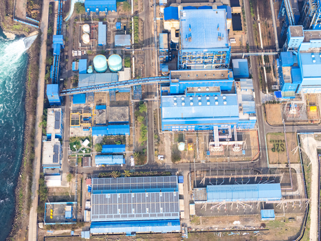 Aerial view of an industrial power plant with blue roofed buildings storage tanks solar panels and electrical infrastructure in Cilacap Selatan Central Java Indonesia.