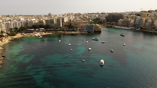 Aerial view of boats anchored in the clear turquoise waters of Spinola Bay surrounded by Mediterranean urban architecture in Malta. Aerial view of boats anchored in the clear turquoise waters of Spinola Bay surrounded by Mediterranean urban architecture in Malta.