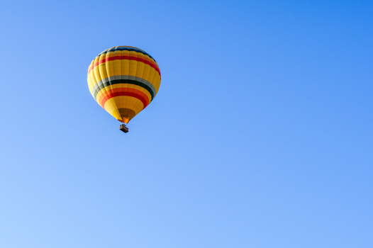 Aerial view of a colorful yellow and red striped hot air balloon floating in a clear blue sky over the landscape of Cappadocia Kayseri Kayseri Turkiye.