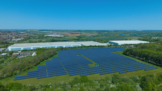Aerial view of a large solar farm with rows of blue photovoltaic panels near industrial warehouses and green fields in Little Irchester England United Kingdom. Aerial view of a large solar farm with rows of blue photovoltaic panels near industrial warehouses and green fields in Little Irchester England United Kingdom.
