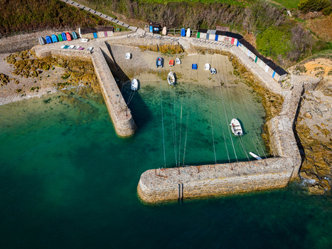 Aerial view of Port Racine a small harbor with stone walls colorful small boats moored in turquoise water and storage sheds along the shore in La Hague Normandie France.