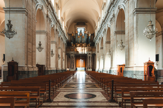 View of serene church interior with symmetric rows of wooden pews and ornate chandeliers casting shadows on the marble floor Taormina Sicily Italy. View of serene church interior with symmetric rows of wooden pews and ornate chandeliers casting shadows on the marble floor Taormina Sicily Italy.