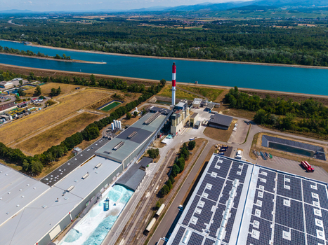 Aerial view of Glas Trosch Alsace SAS industrial facility with a tall chimney warehouse buildings with solar panels and a canal in Hombourg Grand Est France.
