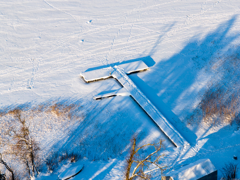 Aerial view of a wooden pier covered in thick snow on a frozen lake with footprints and long shadows in Trakai Vilnius County Lithuania. Aerial view of a wooden pier covered in thick snow on a frozen lake with footprints and long shadows in Trakai Vilnius County Lithuania.