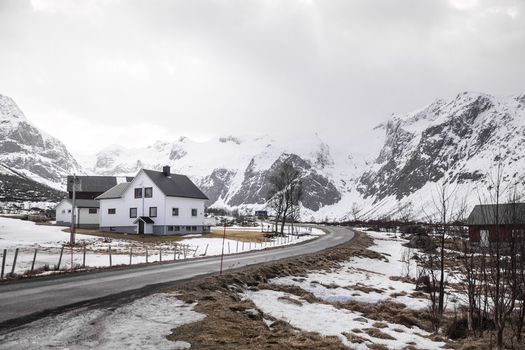 View of a traditional white house nestled in a snowy valley surrounded by majestic snow capped mountains under an overcast sky in Kvaloya Troms Norway. View of a traditional white house nestled in a snowy valley surrounded by majestic snow capped mountains under an overcast sky in Kvaloya Troms Norway.