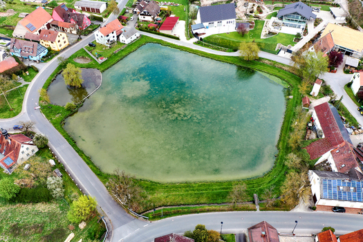 Aerial view of the Ailsbach pond surrounded by residential houses green lawns and local roads in Lonnerstadt Bayern Germany. Aerial view of the Ailsbach pond surrounded by residential houses green lawns and local roads in Lonnerstadt Bayern Germany.