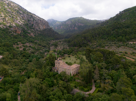 Aerial view of a historic stone manor house nestled in a lush green valley surrounded by forested mountains Valldemossa Balearic Islands Spain.