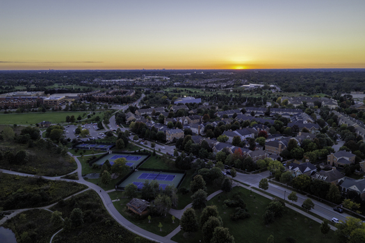Aerial view of a suburban neighborhood in Glenview featuring residential homes tennis courts and green spaces under a golden sunset sky in Glenview Illinois United States. Aerial view of a suburban neighborhood in Glenview featuring residential homes tennis courts and green spaces under a golden sunset sky in Glenview Illinois United States.