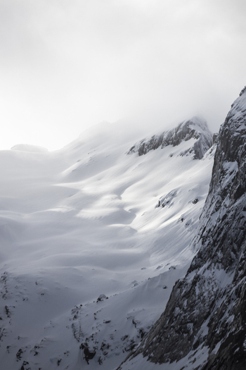 View of snow covered mountain peaks and rugged slopes under a misty sky in Kvaloya Troms Norway. View of snow covered mountain peaks and rugged slopes under a misty sky in Kvaloya Troms Norway.